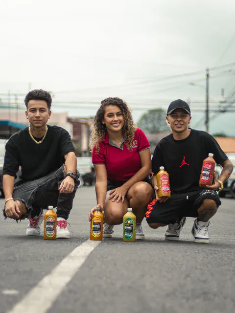Tres personas agachadas en la calle con botellas de Vega's Drinks de varios sabores