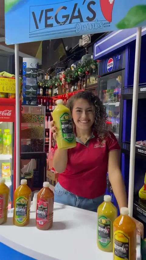 Persona con la polo roja de Vega's muestra una botella en un puesto lleno de botellas de la marca